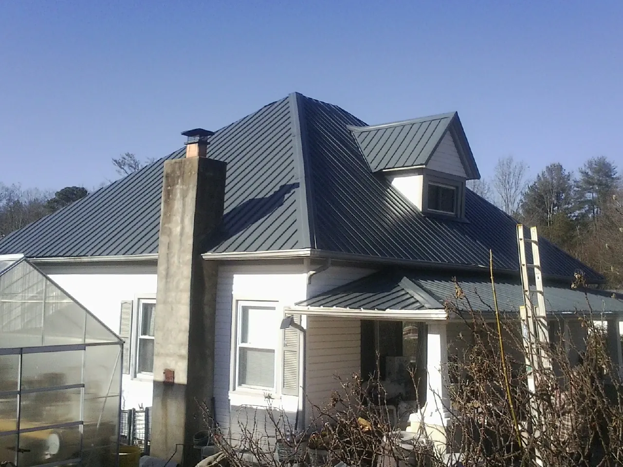 Dark blue standing seam metal roof on a white farmhouse with dormer — Slate & Tile Roof Repair by Roofing Brothers in Beach