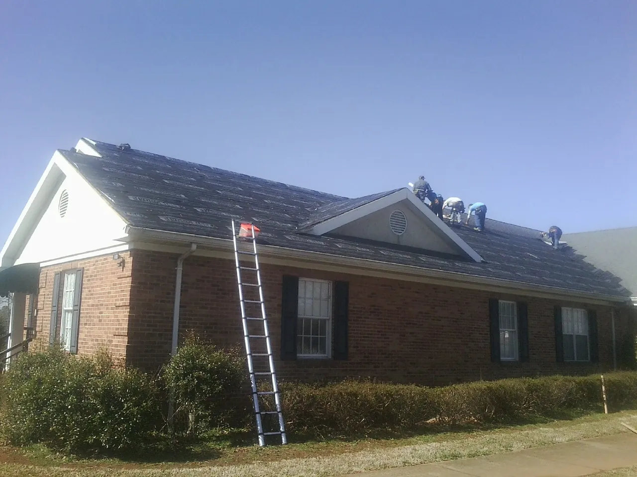 Crew tearing shingles off a brick ranch roof with a ladder set — Emergency Roof Repair work by our crew in Beach
