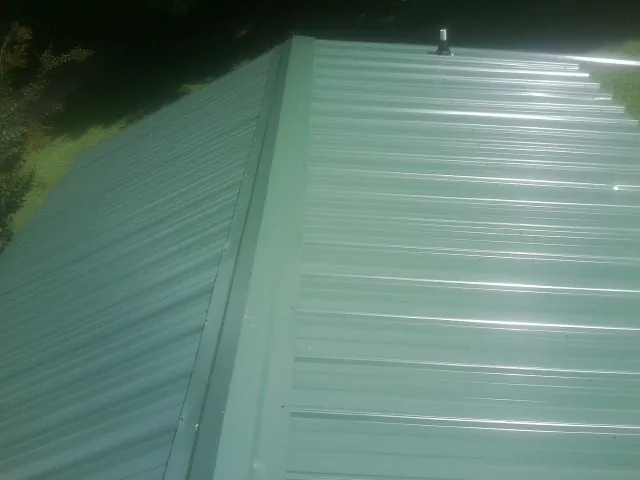 New green metal panels meeting at the ridge of a roof — Flat Roof Repair work by our crew in Beach