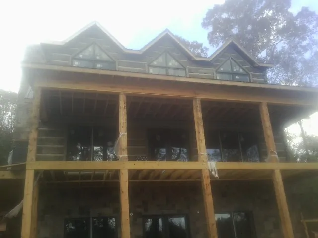 Dormers and porch framing on a large log home under construction — Roof Coating work by our crew in Beach
