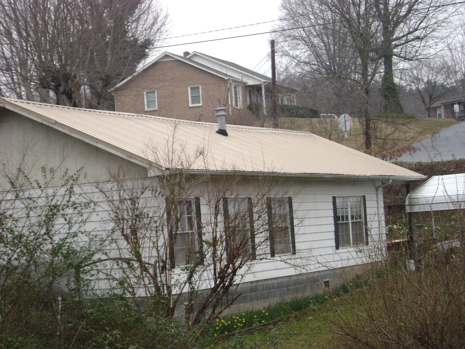 Tan metal roof on a white sided house set into a hillside — Commercial Roofing by Roofing Brothers in Beach