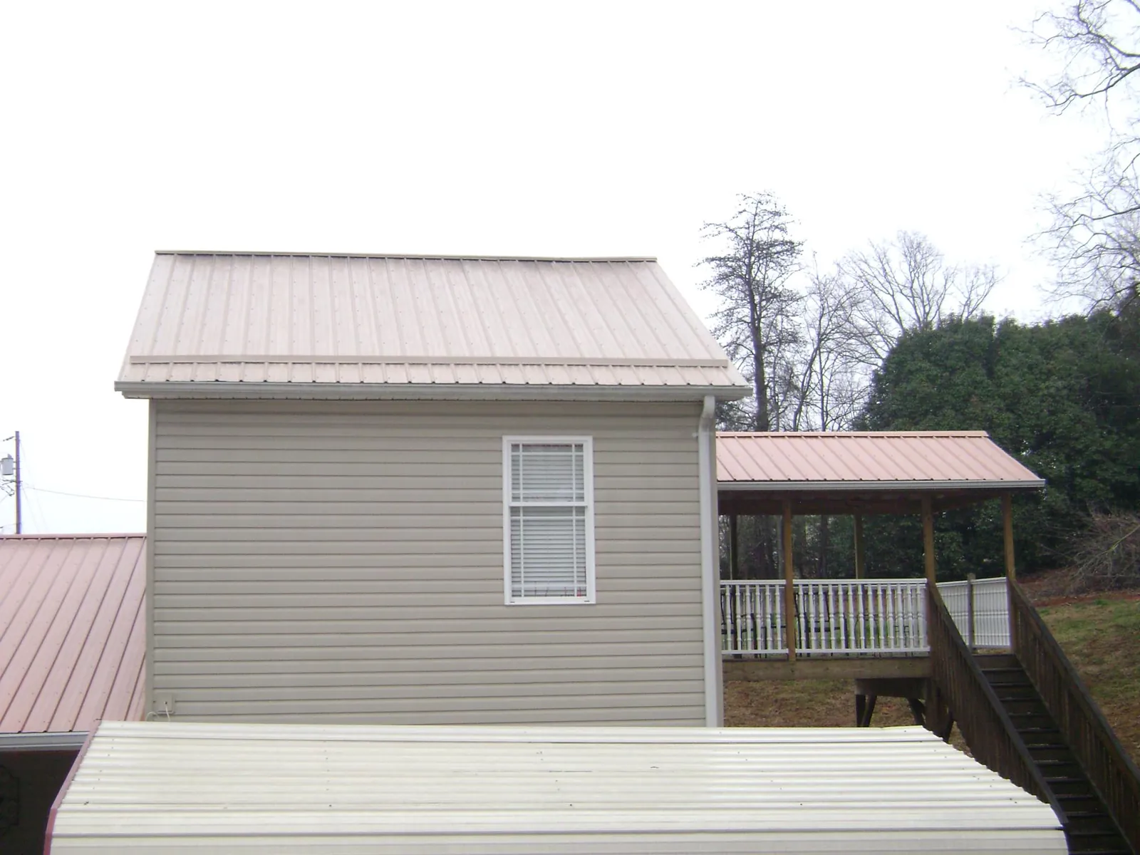 Tan metal roofs on a two story addition and attached porch, from a Roof Replacement job in Beach